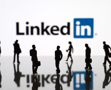 Human figurines standing in front of Apple iPad monitor displaying LinkedIn logo.