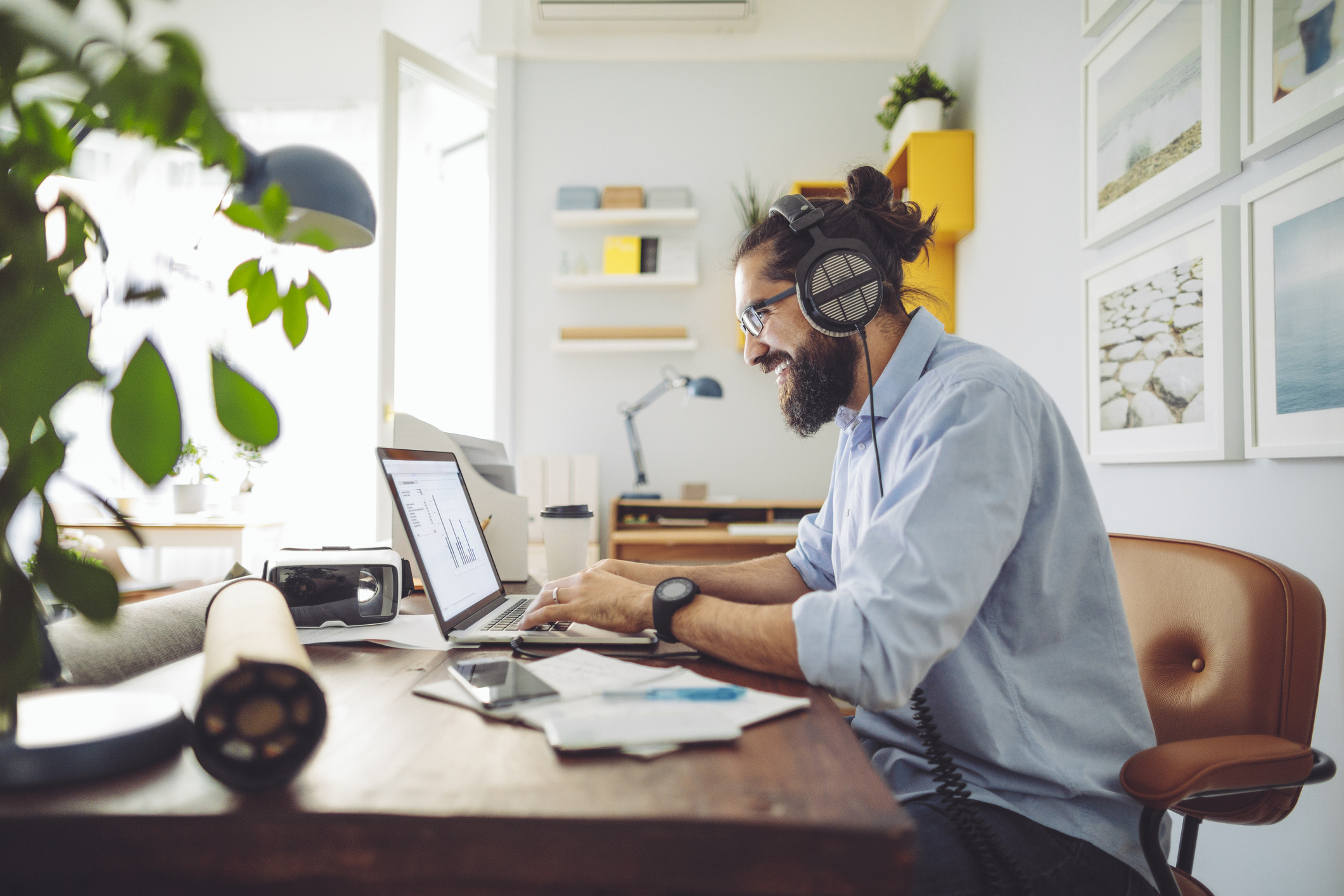 Side view of a man sitting at his home office computer listening to headphones